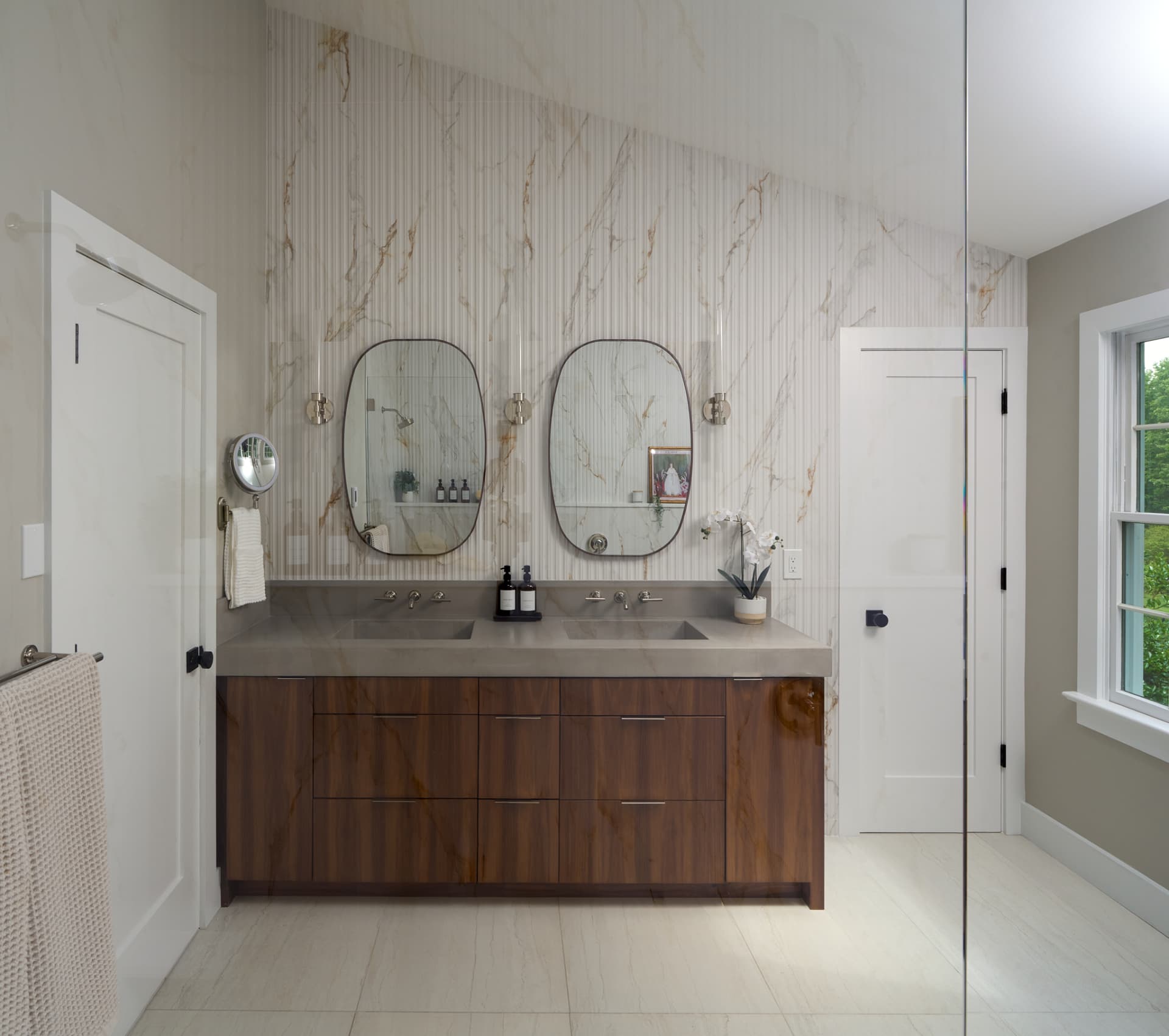 Marble tiled primary bathroom with a walnut vanity and glass shower panel remodeled in Doylestown PA
